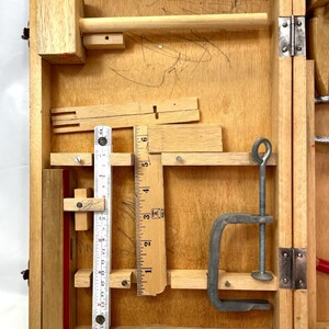 May include: Wooden toolbox with various carpentry tools. Includes a wooden mallet, ruler, clamp, and other small wooden pieces. The box is open, revealing the tools inside. The wood has a natural finish.