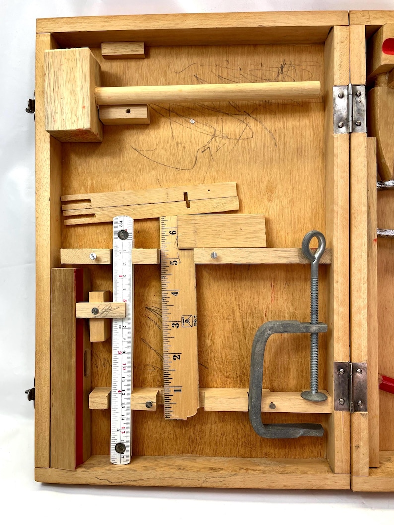 May include: Wooden toolbox with various carpentry tools. Includes a wooden mallet, ruler, clamp, and other small wooden pieces. The box is open, revealing the tools inside. The wood has a natural finish.
