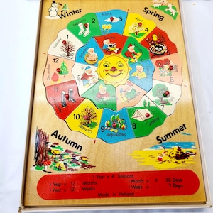 May include: A wooden calendar puzzle featuring a central sun, days of the week, and months of the year with seasonal illustrations. The board includes text: 1 Year = 4 Seasons, 1 Year = 12 Months, 1 Year = 52 Weeks, 1 Month = 30 Days, 1 Week = 7 Days.
