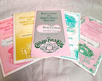 May include: A collection of five Cabbage Patch Kids birth certificate and adoption papers application documents in pink, yellow, and white. Each paper features the Cabbage Patch Kids logo, text, and a cutout window displaying names like Joyvita Fanny.