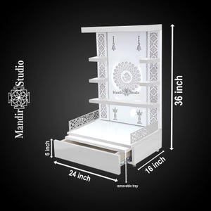 May include: A white wooden cabinet with shelves, a drawer, and decorative cutouts. The cabinet is 36 inches tall, 24 inches wide, and 16 inches deep. It features the text "Mandir Studio" and a removable tray.