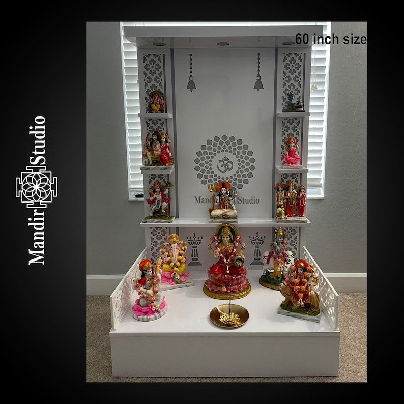 May include: A white wooden altar with multiple shelves, adorned with colorful Hindu deity statues. The altar is 60 inches in size and features intricate cut-out designs and the text "Mandir Studio".