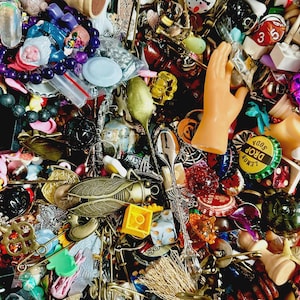 Puede incluir: Una vibrante colección de pequeños objetos decorativos. El surtido incluye piezas de ajedrez, abalorios, cuentas, tapones de botella, cucharas en miniatura y una mano de plástico. Los colores van del dorado y bronce al rojo brillante, azul y verde.