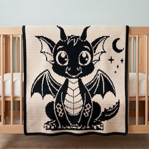 Peut inclure: Une couverture en tricot de couleur crème présentant un grand motif de dragon noir pixélisé. Le dragon a de grands yeux, des ailes et une poitrine écailleuse. À droite du dragon, il y a un petit croissant de lune noir et plusieurs petites étoiles.