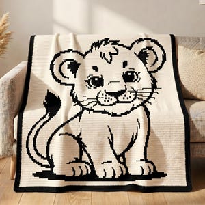 Puede incluir: Una manta rectangular de color crema con una gran ilustración en pixel art negro de un cachorro de león sentado. La manta tiene un borde negro sólido que enmarca el diseño central, el cual muestra al cachorro con ojos grandes y una cola.