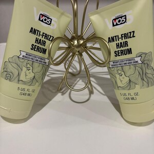 May include: Two tubes of Alberto VO5 Anti-Frizz Hair Serum, each containing 148 ml, are displayed. The tubes are light yellow with black text and a drawing of a woman with wavy hair. They are held by a gold-coloured, decorative metal holder.