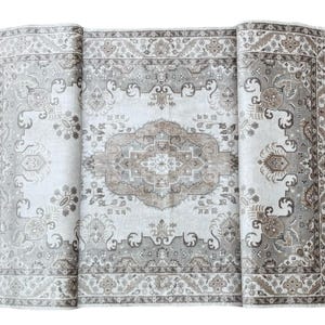 May include: A rectangular area rug featuring a central medallion design in shades of beige, taupe, and cream. The rug displays intricate floral and geometric patterns throughout the field and a wide, detailed border with repeating motifs.