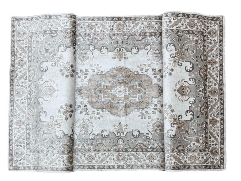 May include: A rectangular area rug featuring a central medallion design in shades of beige, taupe, and cream. The rug displays intricate floral and geometric patterns throughout the field and a wide, detailed border with repeating motifs.