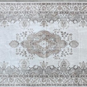 May include: A rectangular area rug featuring a central medallion and intricate floral motifs in shades of beige, taupe, and cream. The design includes a wide decorative border with repeating patterns, all set against a light, neutral background.