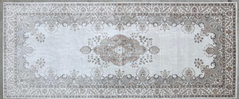 May include: A rectangular area rug featuring a central medallion and intricate floral motifs in shades of beige, taupe, and cream. The design includes a wide decorative border with repeating patterns, all set against a light, neutral background.