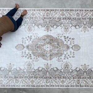 May include: A large rectangular area rug featuring a central medallion and intricate floral border patterns in shades of beige, cream, and soft brown. The rug displays a symmetrical design with detailed motifs throughout the field and edges.