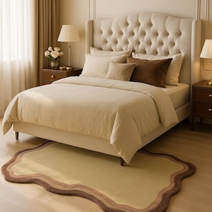 May include: A beige upholstered bed with a tufted headboard, adorned with pillows in varying shades of beige and brown. A matching rug with a wavy border in beige and brown tones sits at the foot of the bed. Two lamps flank the bed.