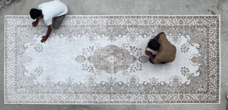 May include: A large rectangular area rug featuring a central medallion and intricate floral border patterns in shades of beige, cream, and soft gray. The design includes symmetrical motifs and detailed scrollwork across the entire surface.