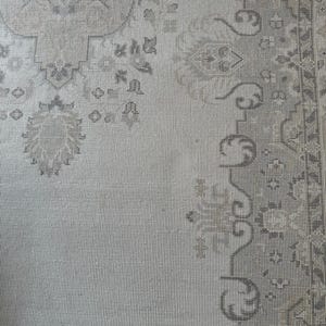 May include: A light gray area rug featuring a detailed woven pattern in darker gray and beige tones. The design includes intricate floral motifs and geometric borders, showcasing a textured surface with a repeating symmetrical layout throughout.