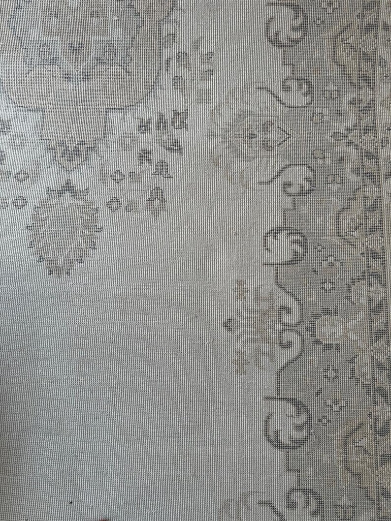 May include: A light gray area rug featuring a detailed woven pattern in darker gray and beige tones. The design includes intricate floral motifs and geometric borders, showcasing a textured surface with a repeating symmetrical layout throughout.