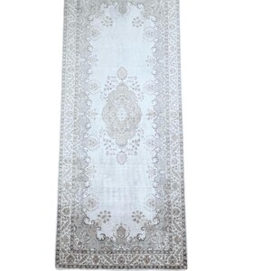 May include: A rectangular runner rug featuring a light gray and beige color palette. The design includes a central medallion surrounded by intricate floral and geometric patterns, enclosed within a detailed border that frames the entire piece.