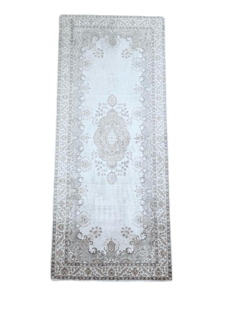 May include: A rectangular runner rug featuring a light gray and beige color palette. The design includes a central medallion surrounded by intricate floral and geometric patterns, enclosed within a detailed border that frames the entire piece.