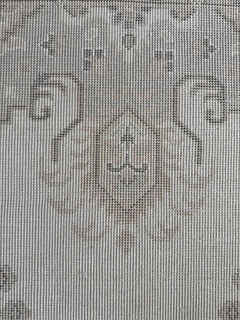 May include: A woven textile featuring a repeating pattern of dark gray and light beige geometric shapes. The design includes a central diamond motif surrounded by symmetrical scrollwork and floral-inspired elements on a textured fabric surface.
