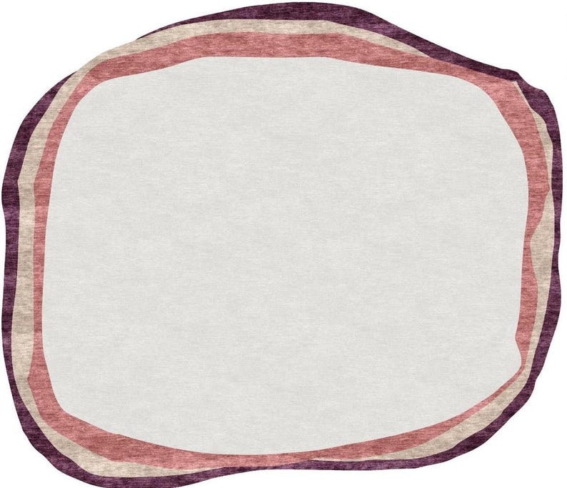May include: A rug with an organic shape and a white center. The border features three bands of color: a dark purple outer edge, a light beige middle band, and a reddish-pink inner band. The rug has a soft, textured appearance.