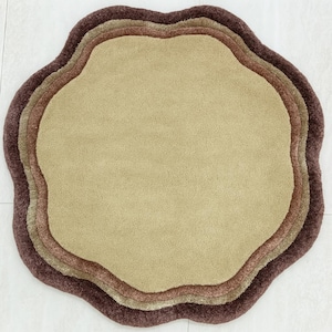 May include: A round, layered rug with a unique, organic shape. The rug features a series of concentric rings in varying shades of brown and beige, creating a textured, inviting surface. The rug's design adds a touch of modern flair to any room.