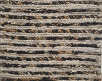 May include: Close-up of a rectangular rug with a woven texture. The rug features horizontal stripes in alternating colours of black, beige, and brown. The rug appears to be made of natural fibres.