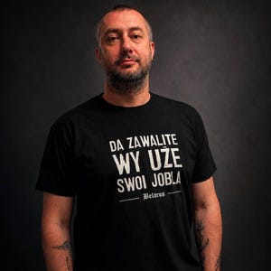 May include: A black short-sleeved t-shirt featuring white distressed text that reads DA ZAWALITE WY UŽE SWOI JOBLA and the word Belarus underlined, worn by a person with visible arm tattoos against a dark, neutral background.
