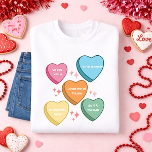 May include: White sweatshirt with colorful heart-shaped graphics. Each heart has a different phrase: "will PCS with u", "b my sponsor", "u had me at Tricare", "ur dependa 4ever", and "do it 4 the BAH".