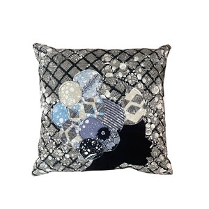 May include: Square decorative pillow with a black and white patterned background. The pillow features a cluster of appliqued circles in shades of blue, gray, and black. The design is a mix of geometric and floral patterns.