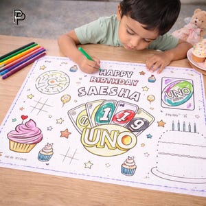 May include: A white placemat with a birthday theme, featuring the text "HAPPY BIRTHDAY SAESHA" and an UNO card game design. The placemat includes a maze, cupcakes, stars, and a birthday cake outline. A child is coloring the placemat with a green marker.