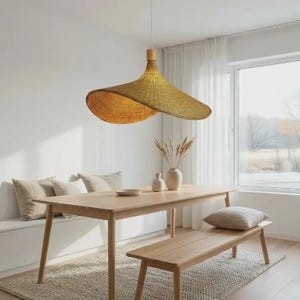 May include: A large, woven pendant light with a wide brim hangs above a wooden dining table. The light fitting has a natural, golden hue and a distinctive, curved design. The dining area also features a bench, rug, and decorative vases.