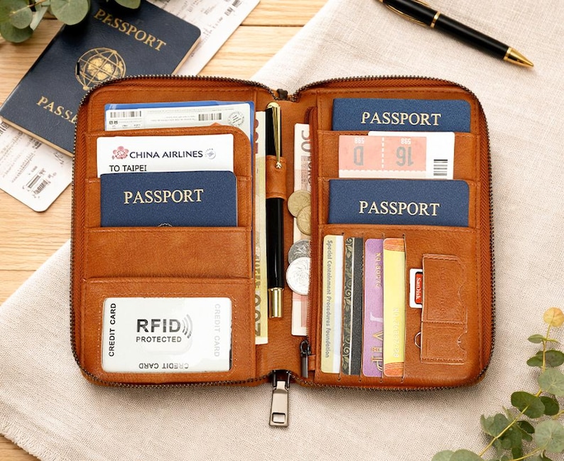 May include: A brown leather travel wallet, open to reveal multiple compartments. Passports, credit cards, tickets, and currency are visible. The wallet has a zipper closure and RFID protection.