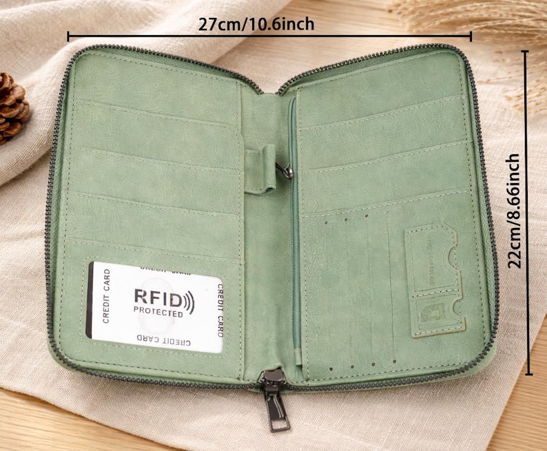 May include: Open, light green wallet with multiple card slots and a zippered closure. The wallet is 10.6 inches wide and 8.66 inches tall. It features a card with "RFID PROTECTED" text. The wallet is made of a soft material and has a dark green zipper.