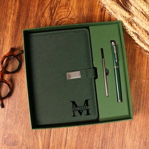 May include: A green leather journal and pen set in a gift box. The journal has a silver clasp and the name "MICHAEL" is printed on the front. The set includes a pen and a pen refill.