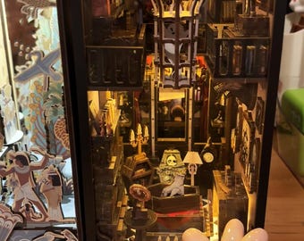 Może przedstawiać: Szczegółowa miniaturowa diorama pokoju z trumną, szkieletem i witrażem. Diorama jest oświetlona ciepłymi światłami, tworząc upiorną atmosferę. Ceramiczna dłoń ze szwami znajduje się na pierwszym planie.