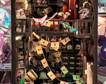 Könnte beinhalten: Detailliertes, beleuchtetes Diorama einer magischen Bibliotheksszene. Die Miniaturwelt zeigt Regale mit Büchern, Schriftrollen und dekorativen Gegenständen. Eine Figur in einem Gewand steht in der Mitte. Dekorative Elemente sind hängende Briefe und ein sternförmiges Licht.