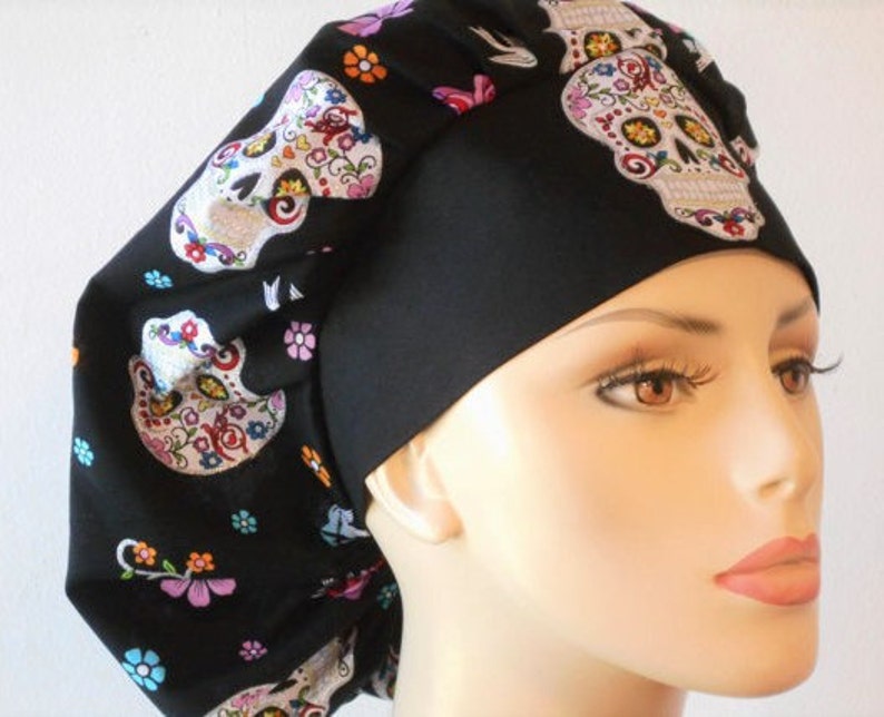 May include: Black scrub hat with a colorful sugar skull pattern. The hat has a black band and a tie at the back.