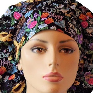 May include: A black surgical scrub cap with a floral pattern featuring sunflowers, roses, and butterflies. The cap has the words "Be Happy" and other script. The cap is designed to cover the hair during medical procedures.