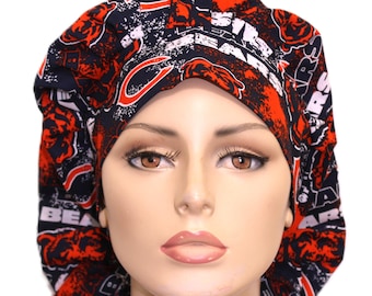 May include: A scrub cap featuring a repeating pattern of the Chicago Bears logo and text in navy blue, orange, and white. The fabric hat has a gathered, rounded crown and a wide, structured front band that sits across the forehead area.