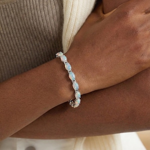 May include: A silver bracelet with oval opals. The opals are arranged in a line, creating a delicate design. The bracelet is worn on a wrist, showing its subtle sparkle and colour. The bracelet is approximately 17 cm in length.