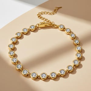 May include: A gold-colored bracelet featuring a series of round, clear gemstones set in individual bezels. The bracelet has a delicate chain and a secure clasp. The gemstones are evenly spaced, creating a sparkling, elegant accessory.