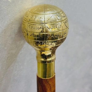 Puede incluir: Bastón con empuñadura de globo de latón, grabado con continentes y océanos. El eje es de madera oscura con un collar de latón. El bastón mide aproximadamente 90 cm de largo.