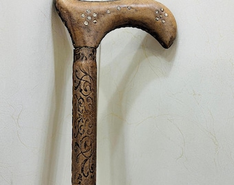 May include: A brown walking cane with a curved handle. The handle is adorned with small, sparkling embellishments and a textured leather finish. The shaft features intricate, embossed floral patterns, adding to its decorative appeal.
