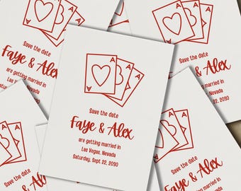 May include: White wedding save-the-date cards with a red playing card design featuring hearts and the text "Faye & Alex". The cards announce a wedding in Las Vegas, Nevada, on September 22, 2030.