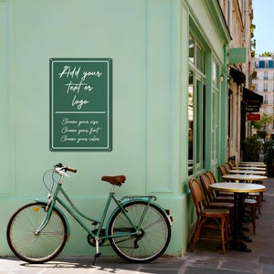 May include: A teal bicycle with a brown seat is parked next to a green wall. A rectangular sign on the wall reads "Add your text or logo" and "Choose your size, font, and color."