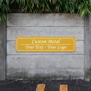 May include: A rectangular, mustard-yellow metal sign with rounded corners is mounted on a concrete wall. The sign features the text "Custom Metal Your Text - Your Logo" in a white, elegant font. The sign is secured with small rivets.