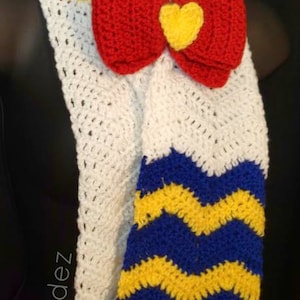 May include: White crocheted scarf with a red and yellow bow and blue and yellow chevron stripes.