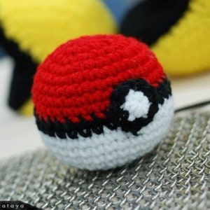 May include: A red, white, and black crocheted Poké Ball. The Poké Ball is a popular item in the Pokémon franchise.