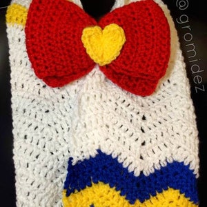 May include: A white crocheted scarf with a red bow and a yellow heart in the center. The scarf has blue and yellow stripes at the bottom.