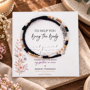 May include: A beaded bracelet featuring black, white, and metallic gold beads arranged in a pattern, displayed on a white card with the text I'D HELP YOU Bury the body, THANK YOU FOR BEING my partner in crime, and ARDENT FONDNESS MORSE CODE BRACELET.