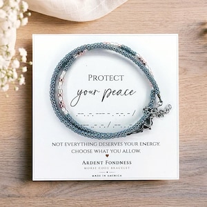 May include: A Morse code bracelet featuring small slate blue and metallic rose gold beads on a white display card. The card reads PROTECT your peace, NOT EVERYTHING DESERVES YOUR ENERGY, CHOOSE WHAT YOU ALLOW, ARDENT FONDNESS MORSE CODE BRACELET.